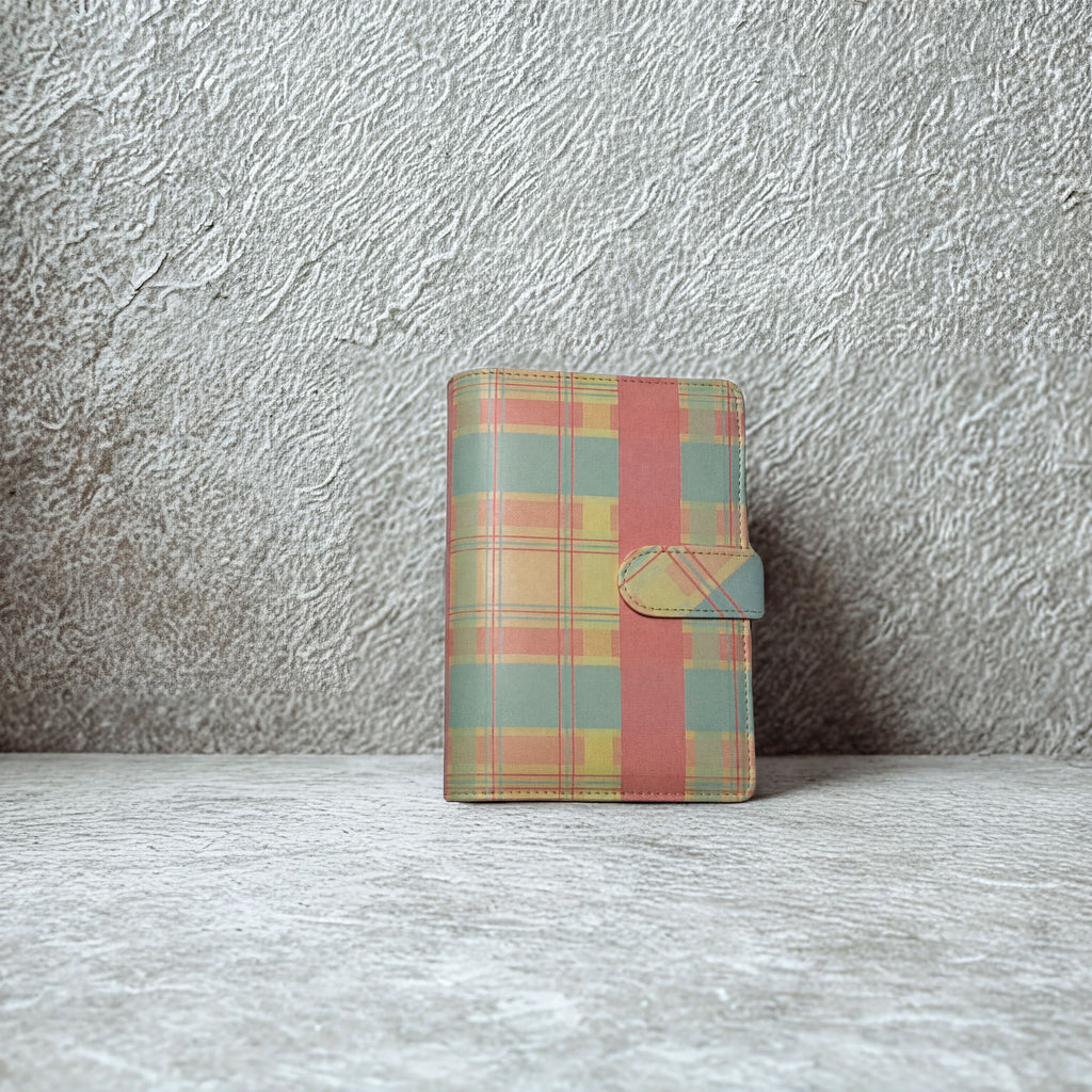 Plaid patterned notebook with pink stripe and snap closure on textured surface