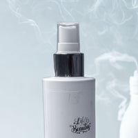 A white spray bottle with a black cap, against a blue background with smoke or steam.