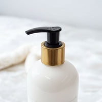 A white pump bottle with a black pump and gold-colored cap is shown against a white background.