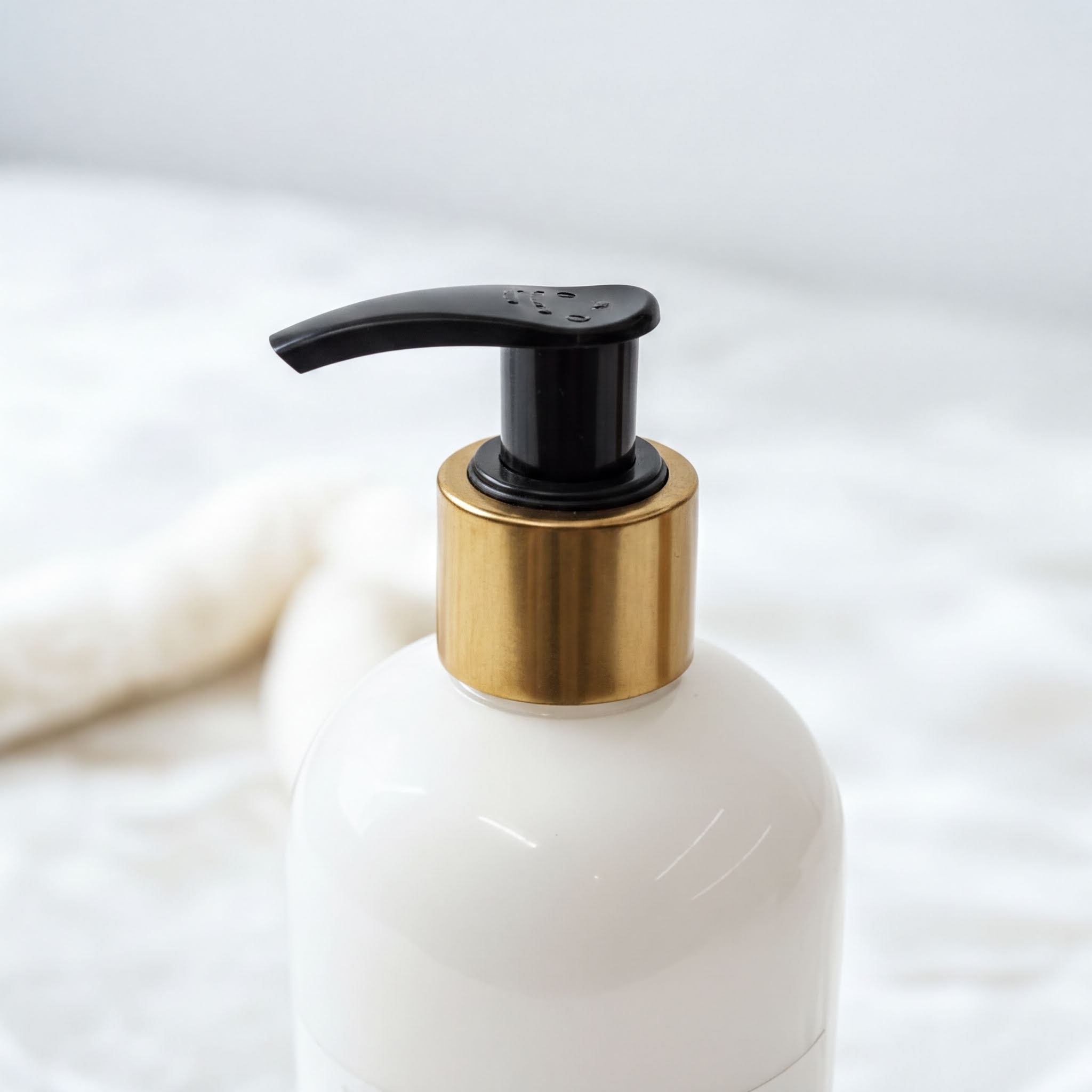 A white pump bottle with a black pump and gold-colored cap is shown against a white background.