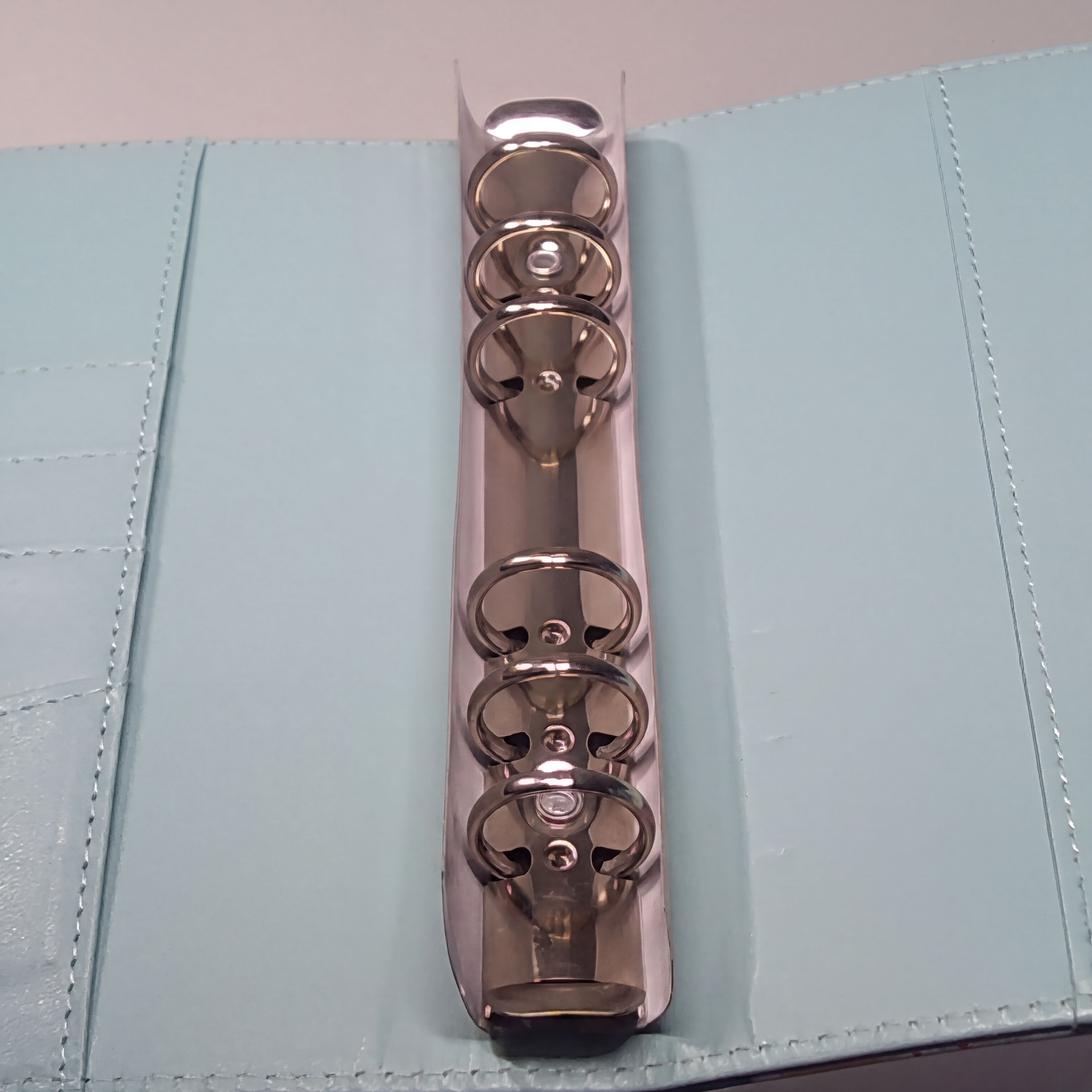 Shiny rose gold binder rings on light blue stitched cover