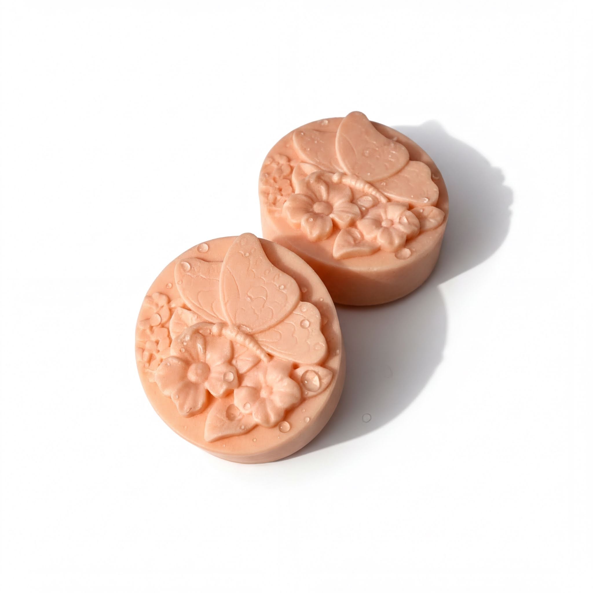Two round, pink soap bars with intricate floral designs on them.