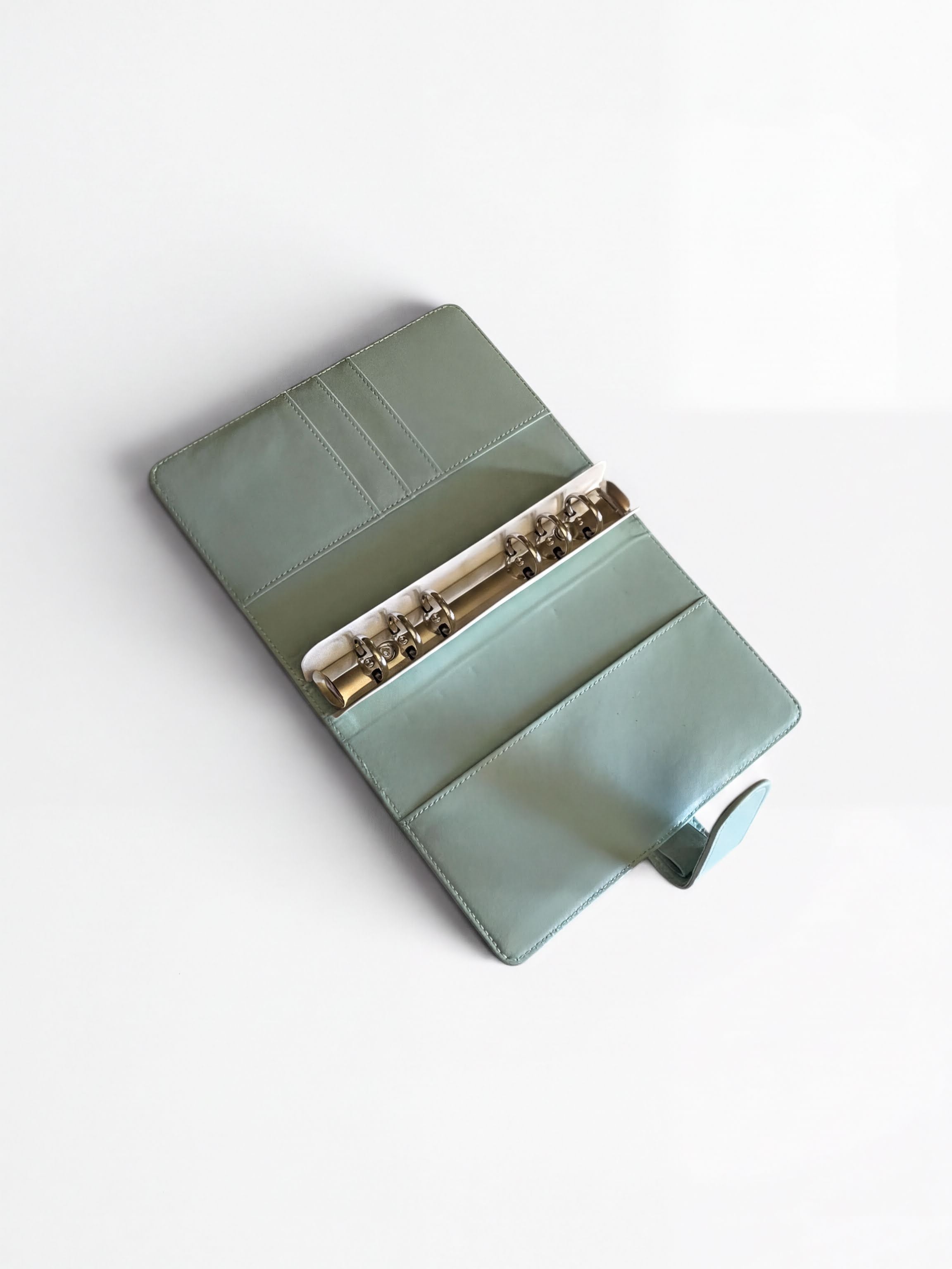 A mint green leather binder with a metal ring cover and a metal ring inside, placed on a white surface.