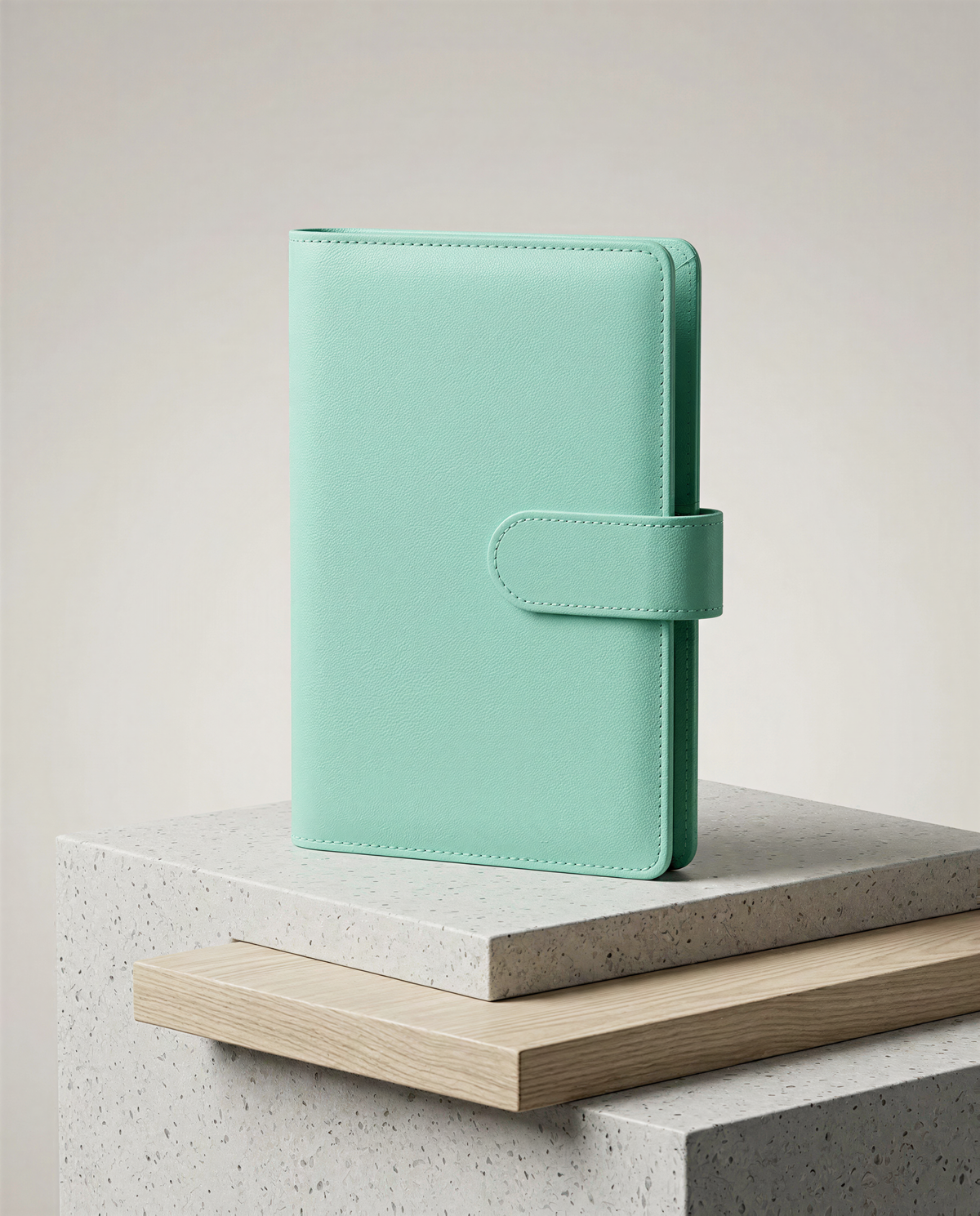 A mint green leather wallet or book cover is displayed on a wooden platform against a plain background.