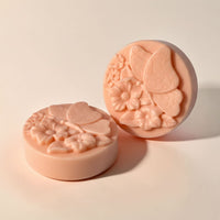two round, pink soap bars with intricate floral designs on them.