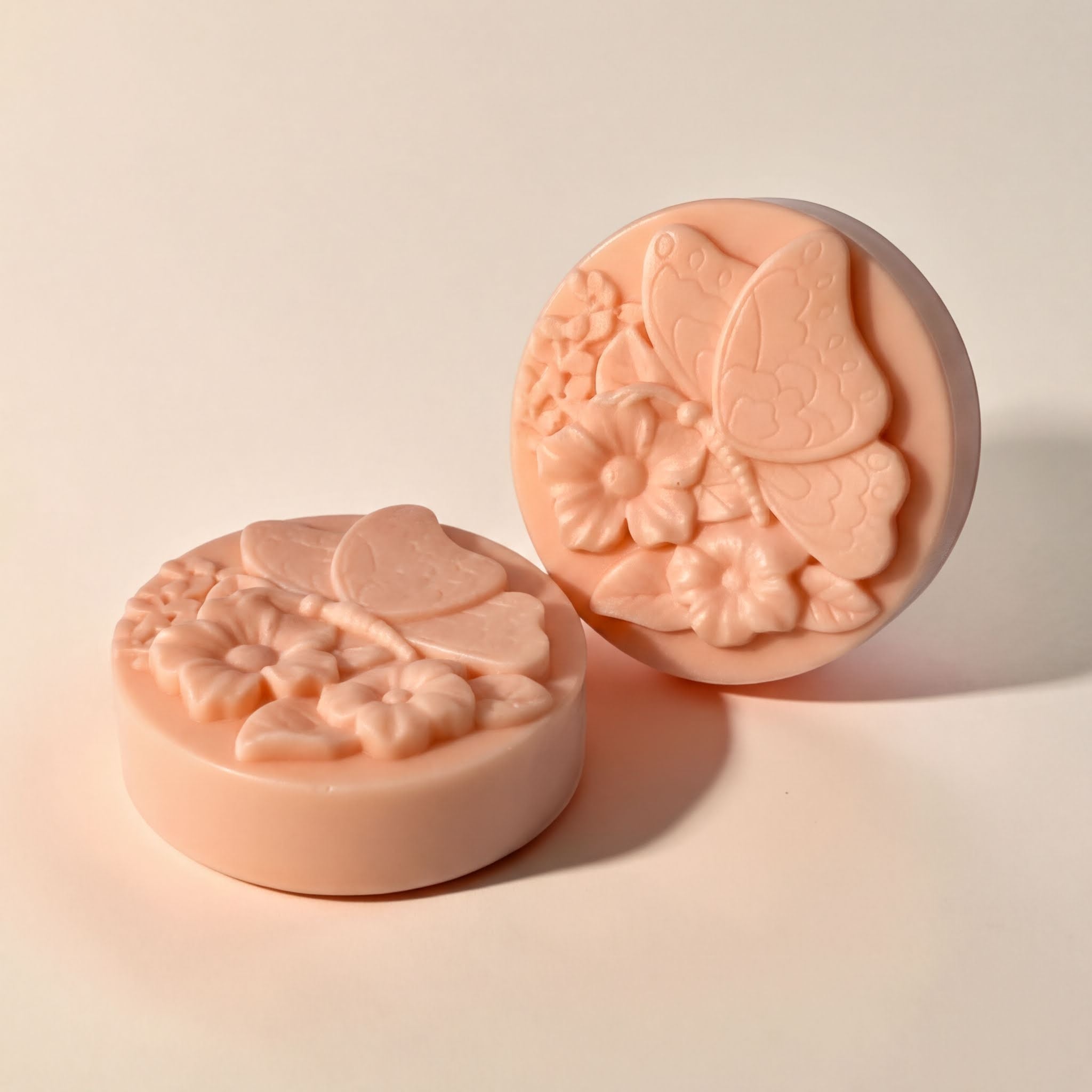 two round, pink soap bars with intricate floral designs on them.