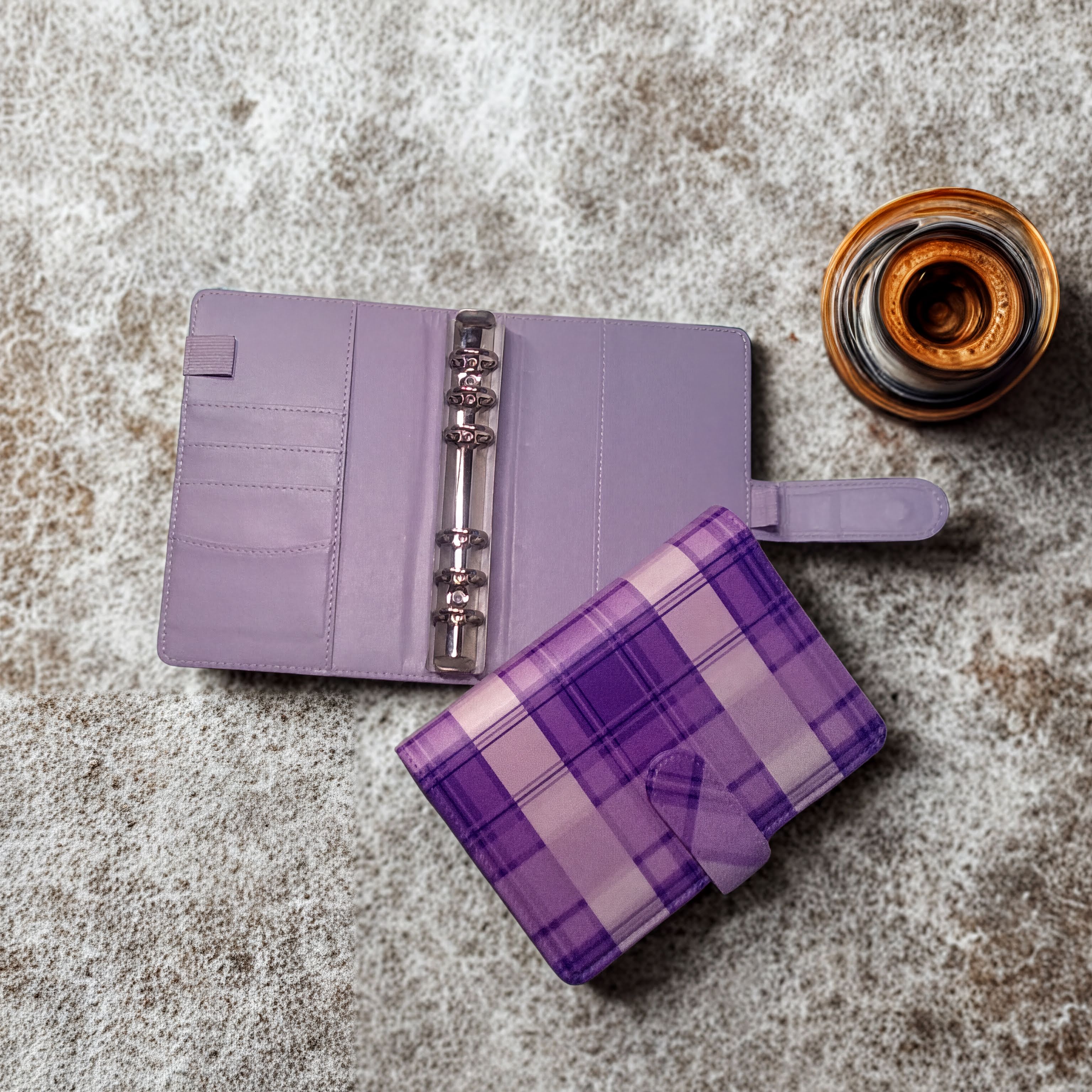Purple plaid planner with open ring binder and glass of amber liquid on textured surface