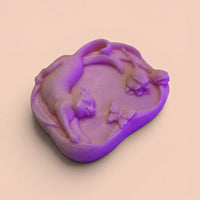 A purple, hand-shaped soap with a cat and butterflies on it, sitting on a light peach background.