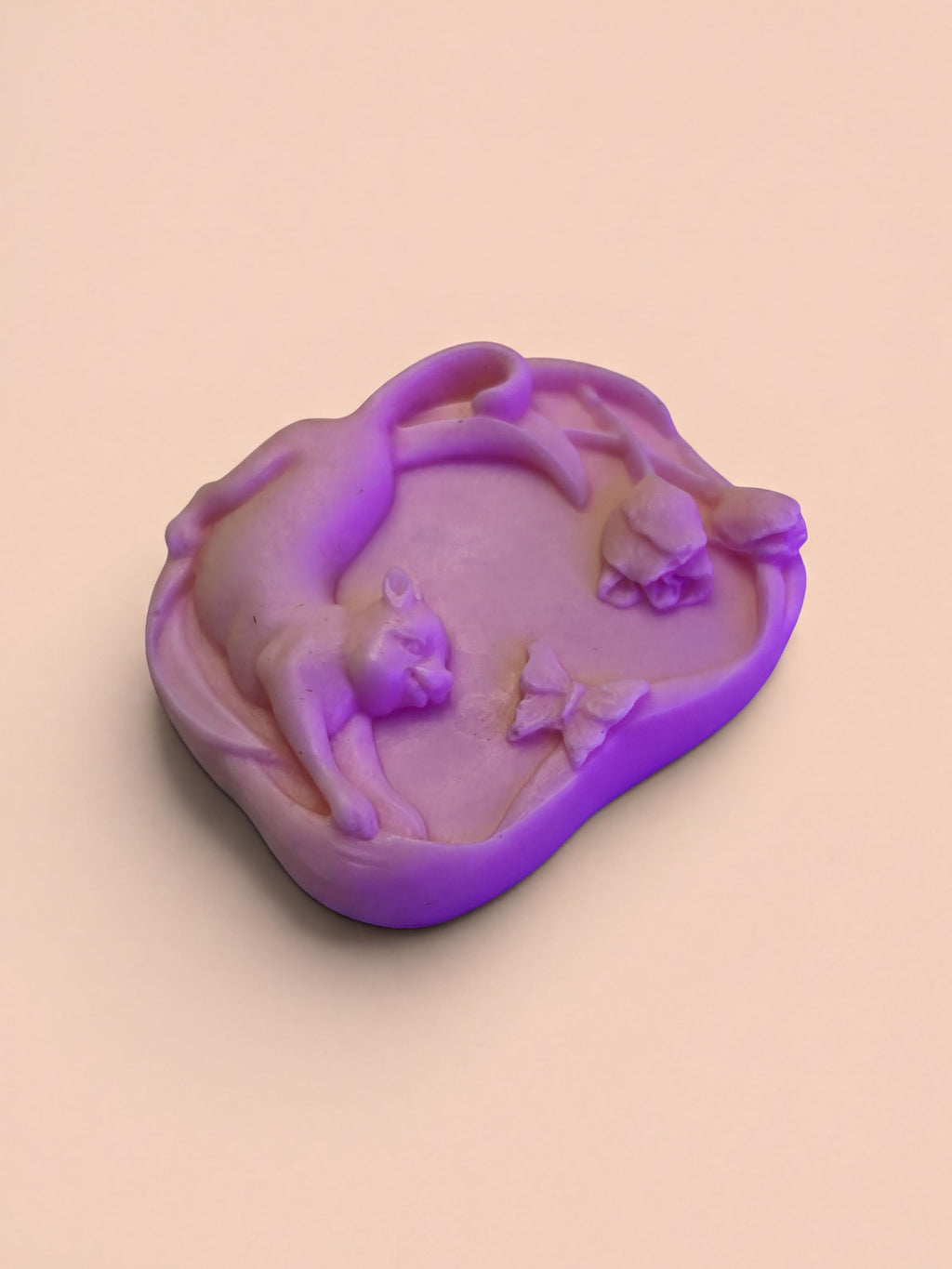 A purple, hand-shaped soap with a cat and butterflies on it, sitting on a light peach background.