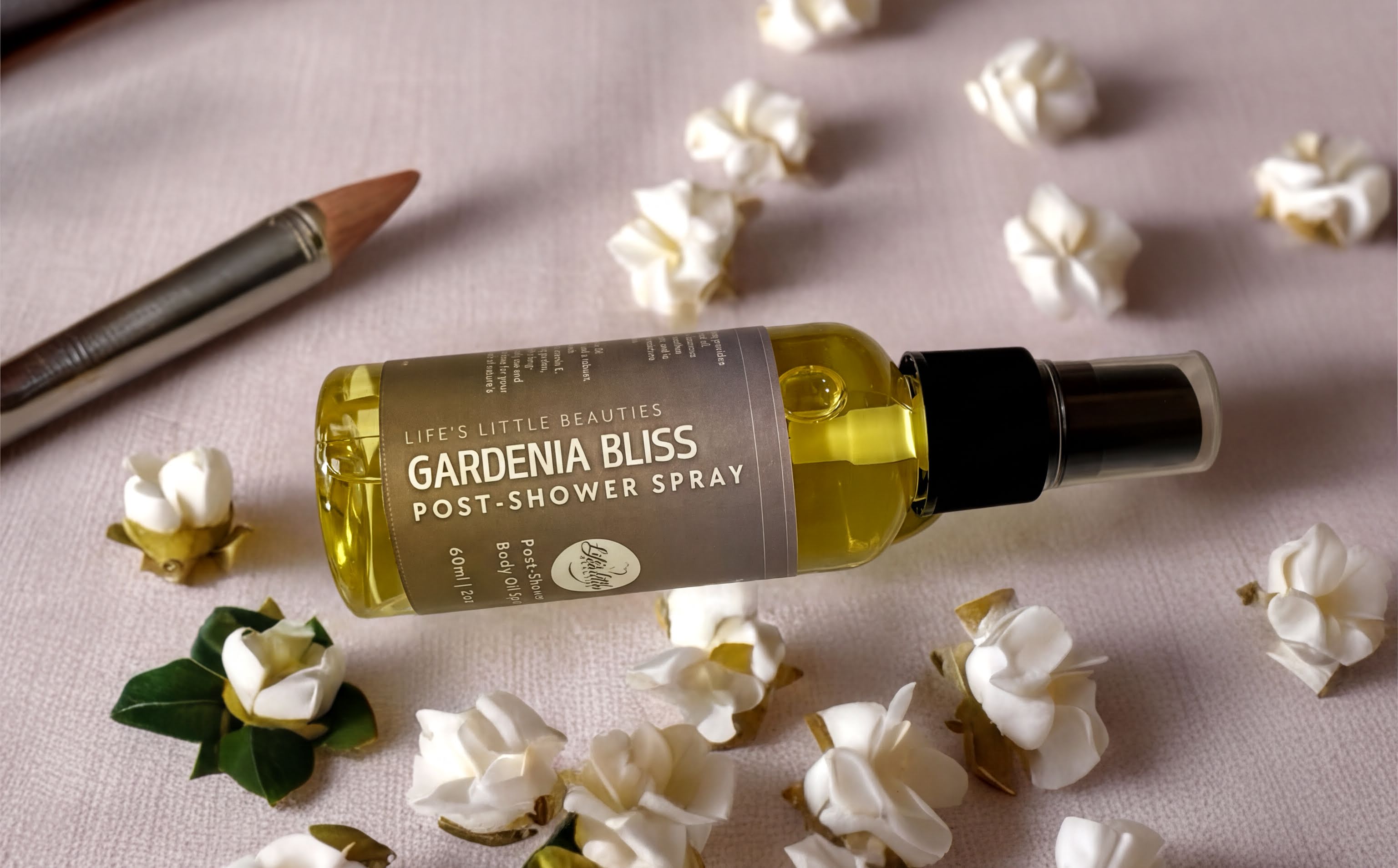 a bottle of Gardenia Bliss Post-Shower Spray surrounded by white flowers and leaves on a table.