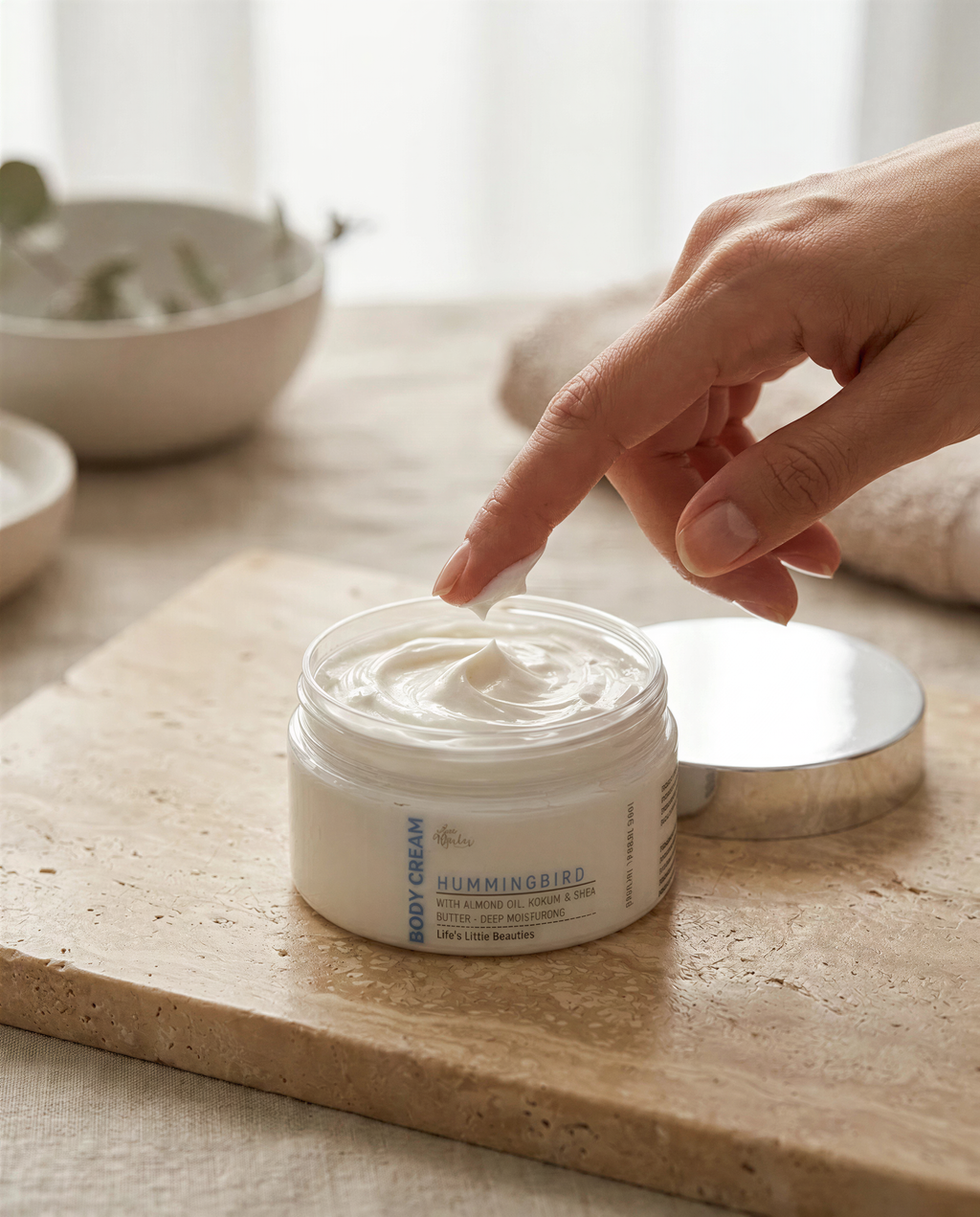 A hand applying body cream to a jar on a wooden surface.