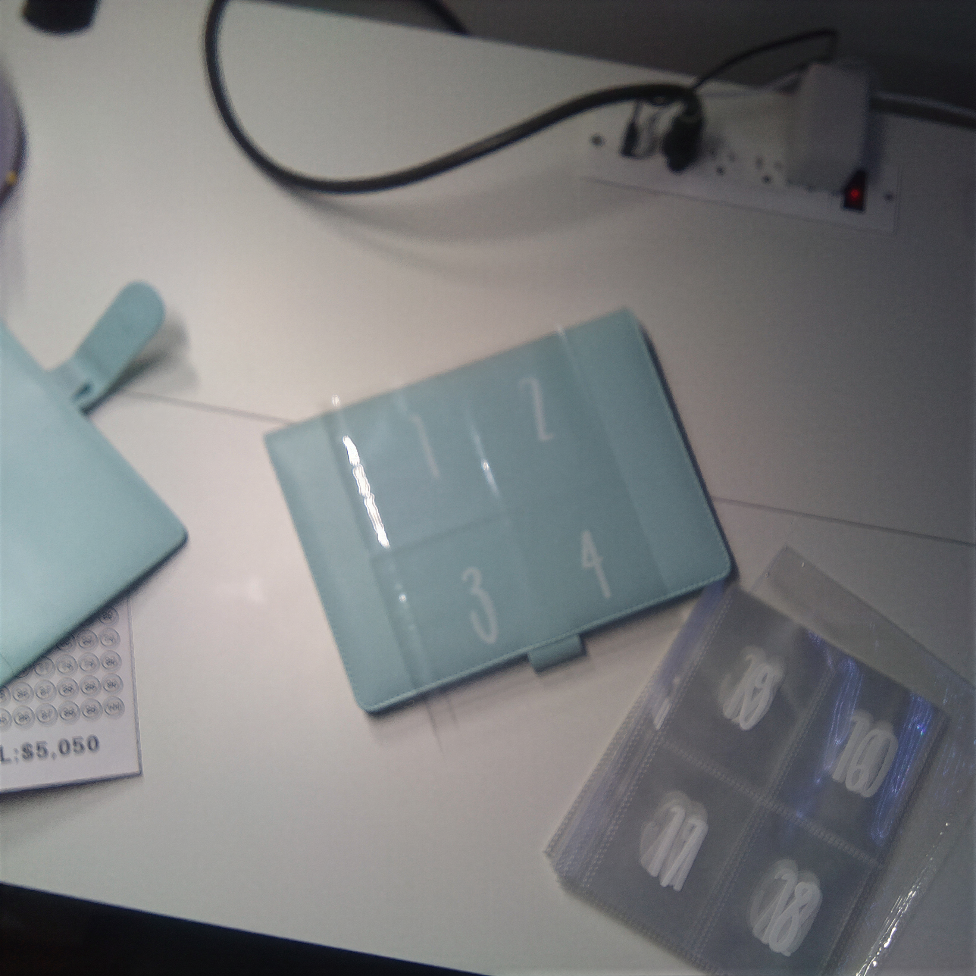 Light blue numbered tablet case and clear organizer on white desk with cables