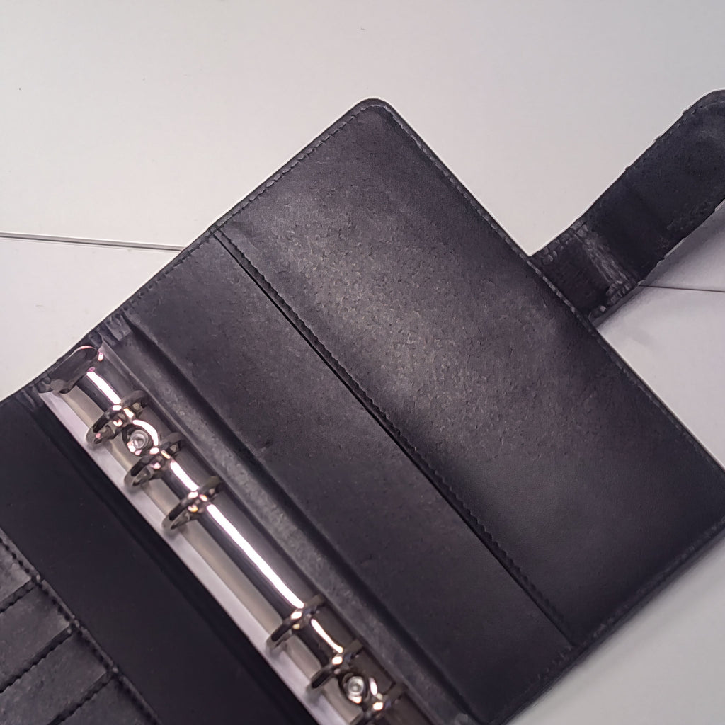 Black leather-bound planner with silver rings and stitched edges on white surface
