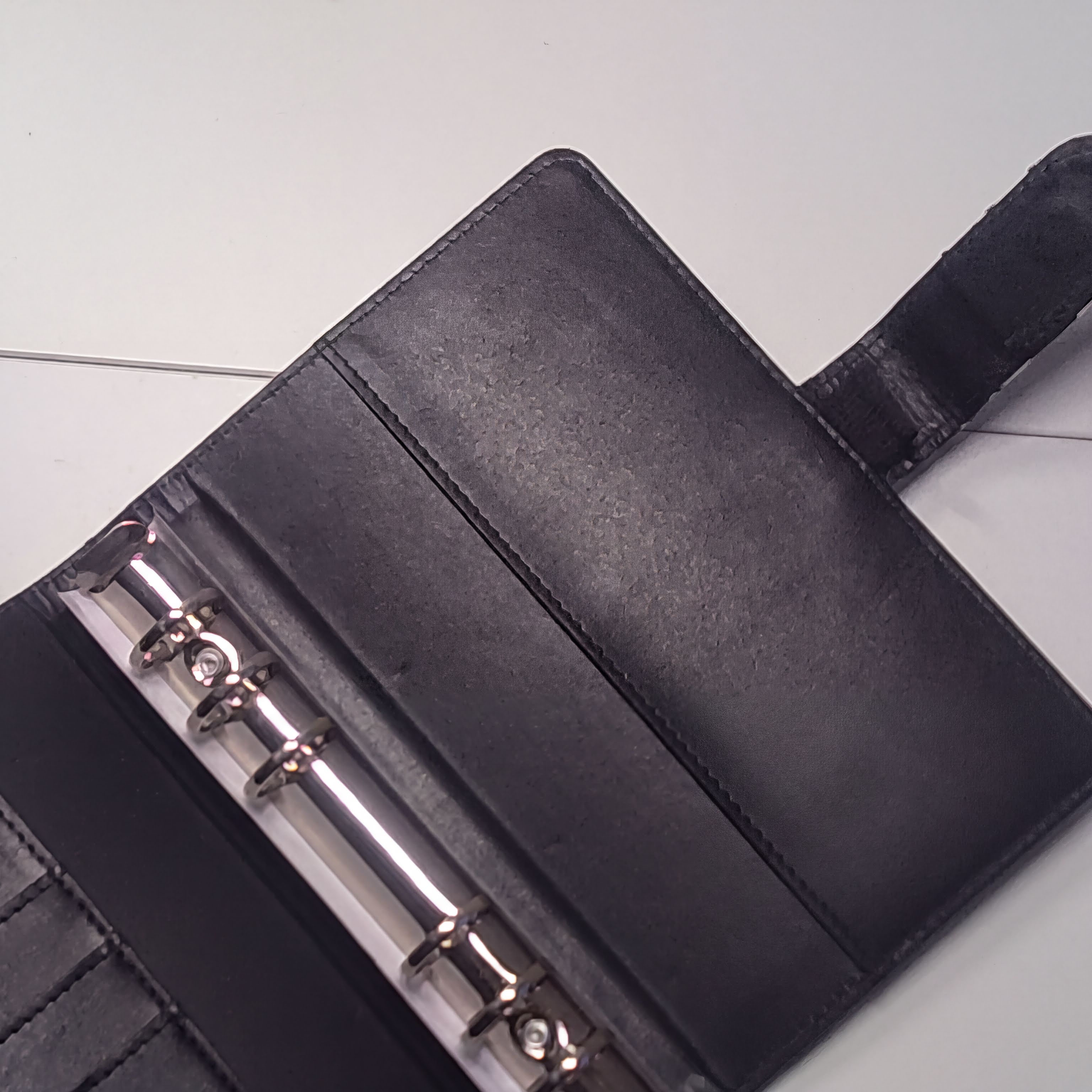 A black leather-bound notebook or binder with metal rings, resting on a white surface.