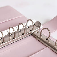 A close-up view of a metal ring mechanism on a pink leather-like surface.