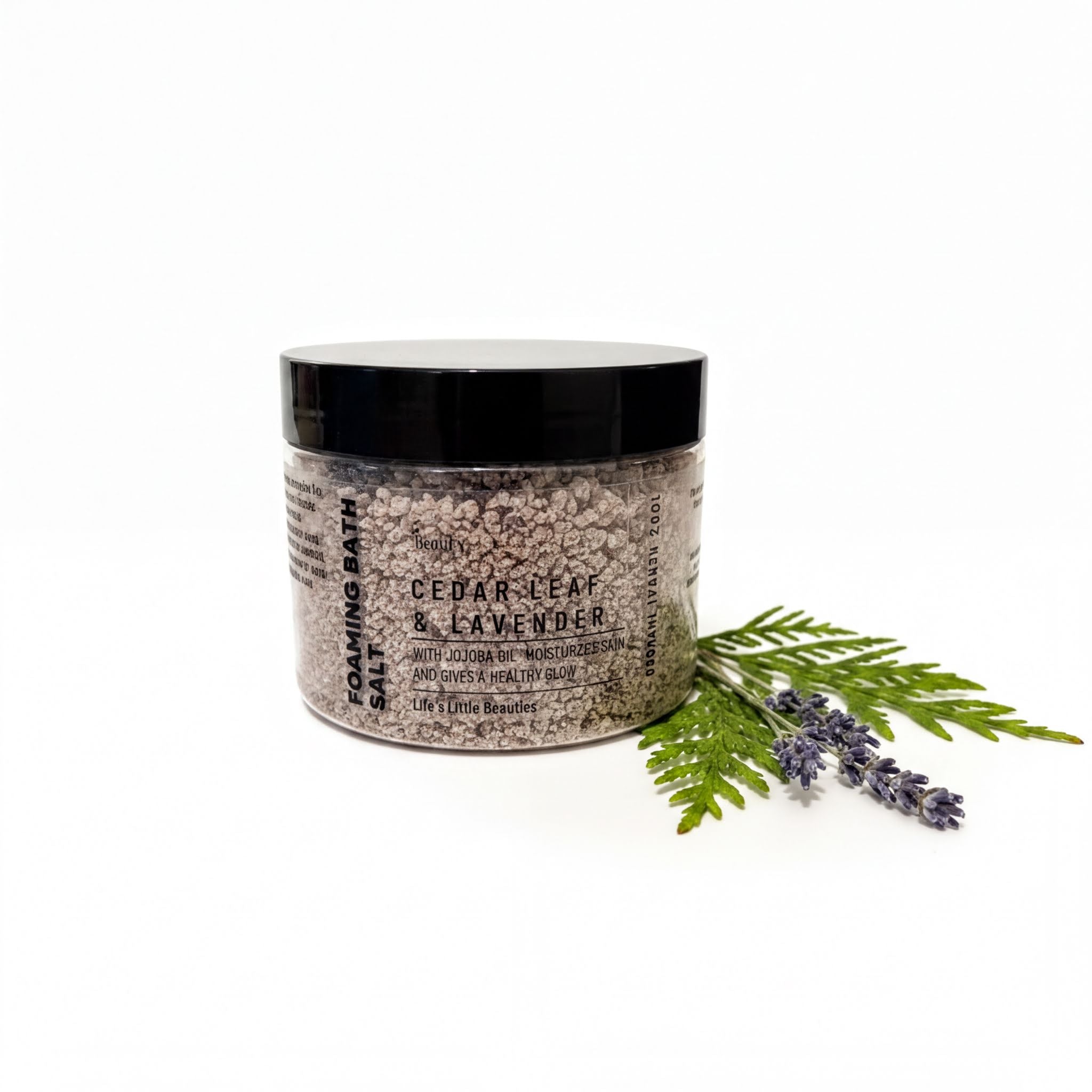 A jar of Cedar Leaf & Lavender Soaking Bath Salt, surrounded by a sprig of lavender and a fern leaf, against a white background.