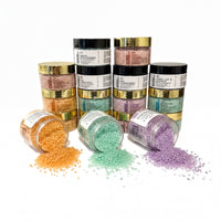 a collection of jars and containers filled with various colored bath salt crystals, including orange, green, purple, and lavender, spilling out onto a white background.