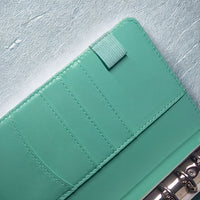 A mint green leather wallet or purse with a zipper closure and a small zipper pull on the top.