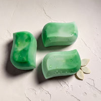 Three green rectangular bars of soap are arranged on a white surface, with one bar resting on its side and two bars placed upright.