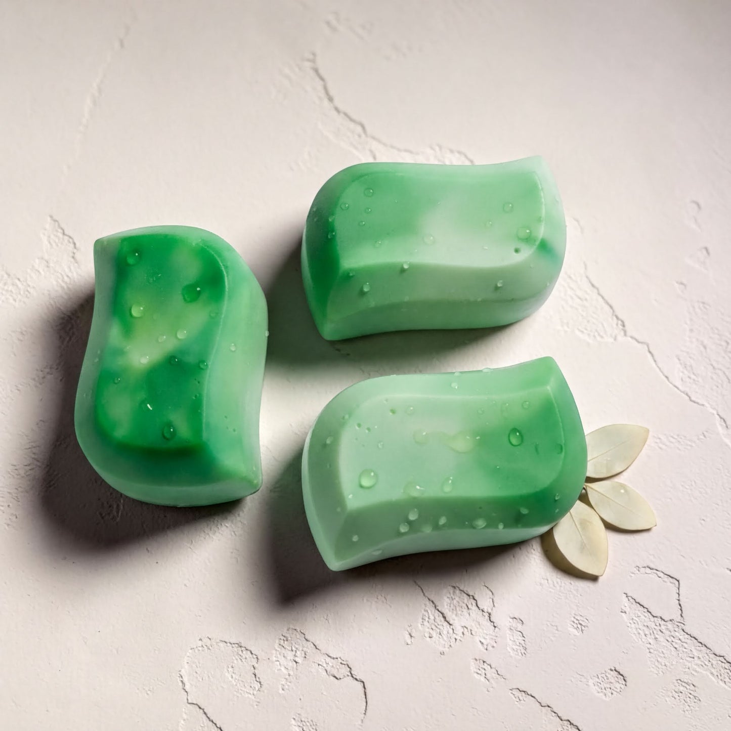 Three green rectangular bars of soap are arranged on a white surface, with one bar resting on its side and two bars placed upright.