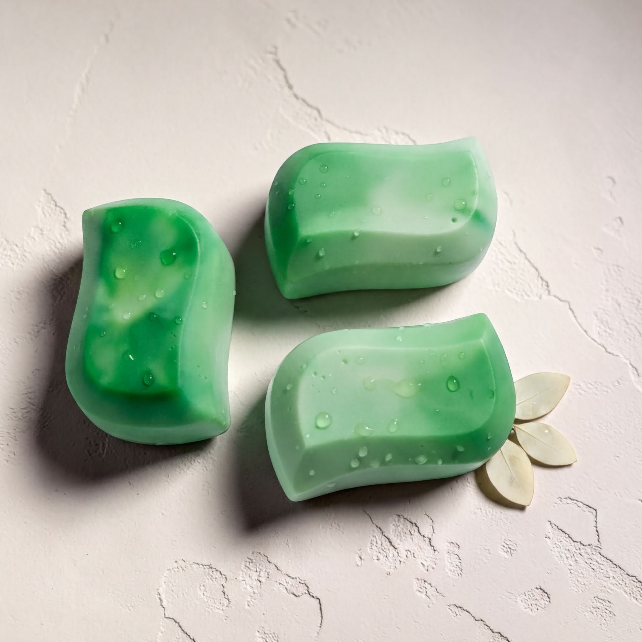 Three green rectangular bars of soap are arranged on a white surface, with one bar resting on its side and two bars placed upright.
