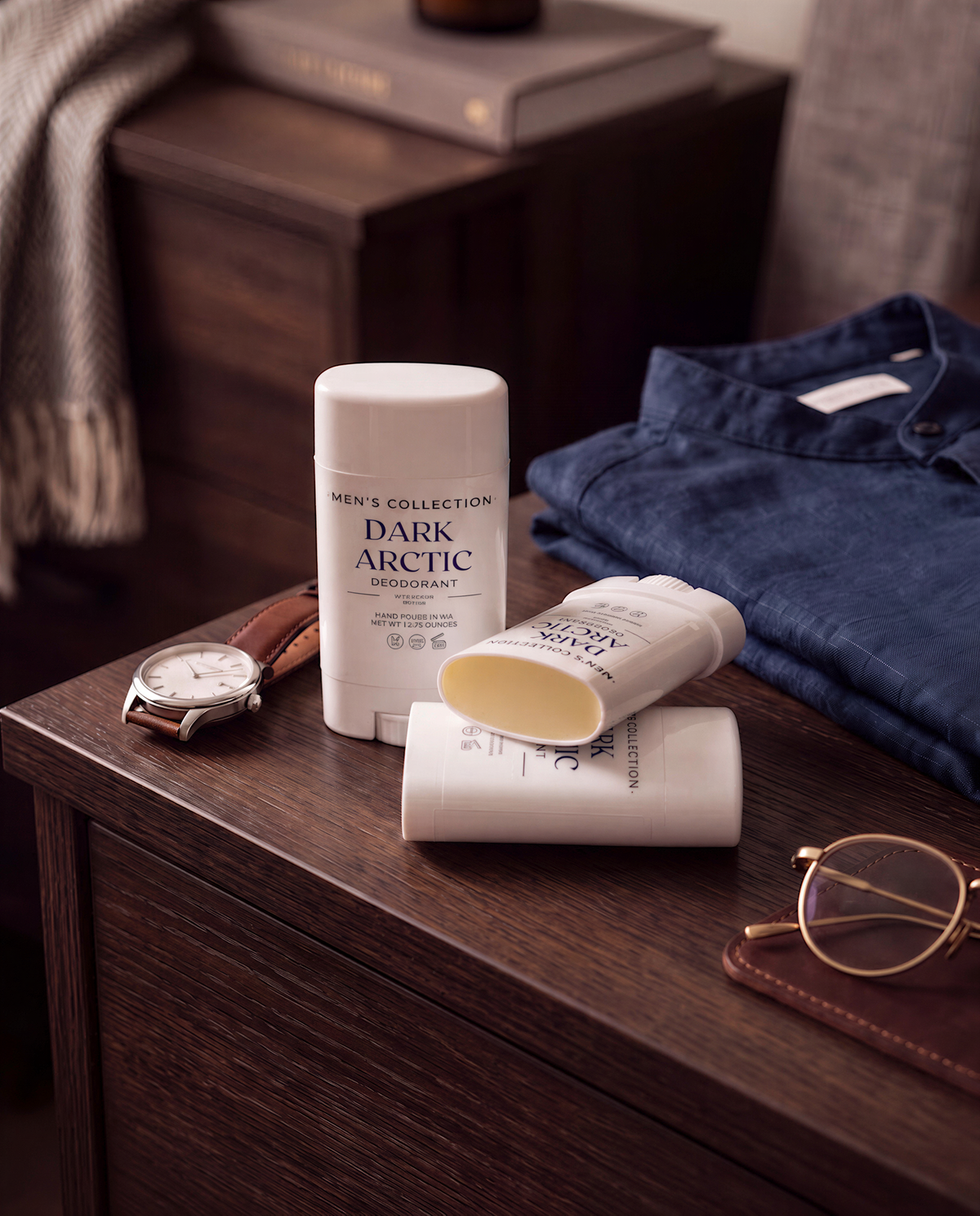 a collection of men's grooming products, including a deodorant stick, a watch, and a pair of glasses, arranged on a wooden surface.