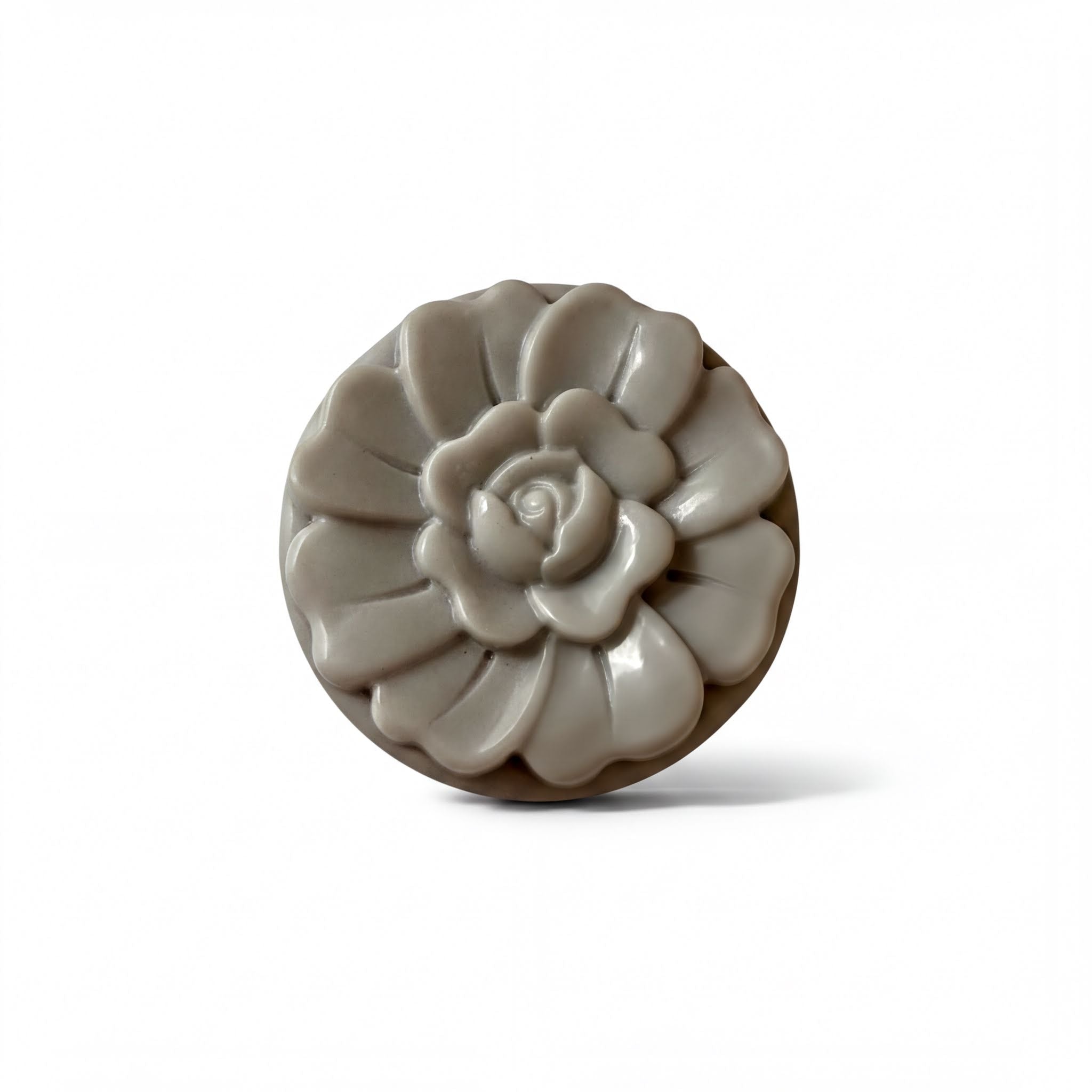 A gray, round soap with a flower-shaped design on it.