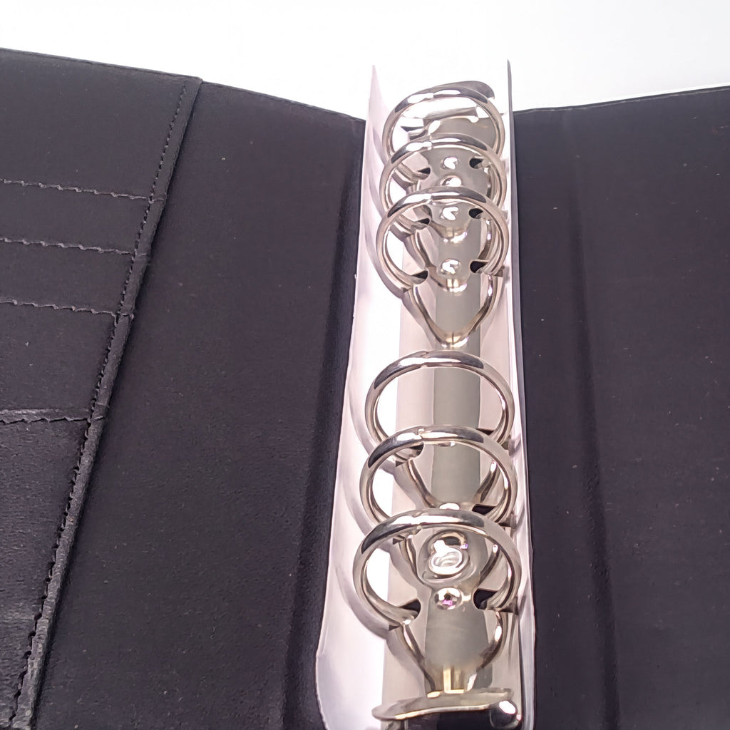 Shiny silver binder rings on black textured cover, close-up view