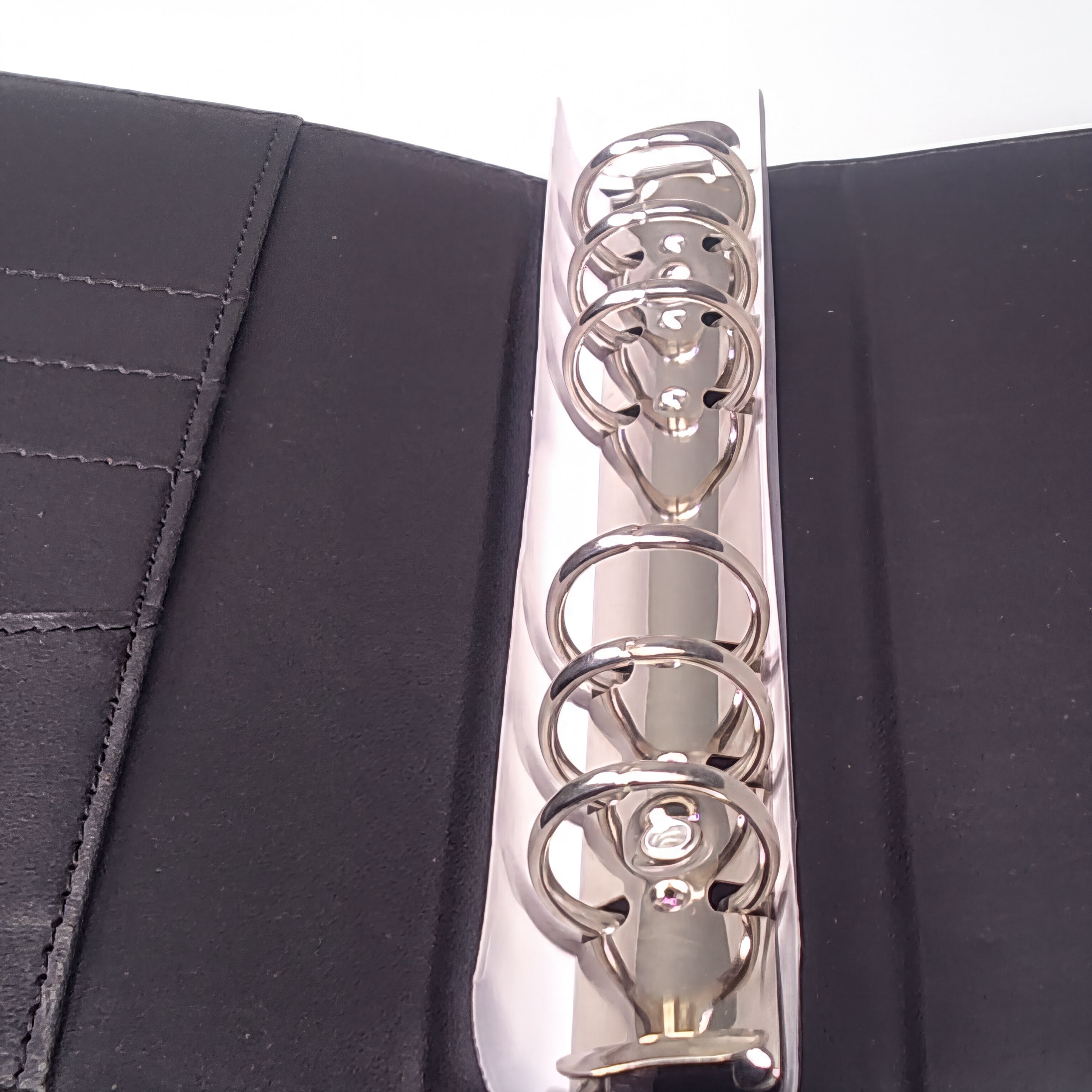Shiny silver binder rings on black textured cover, close-up view