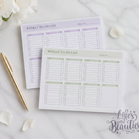 two weekly to-do lists on a marble surface, with a pen and a flower nearby.