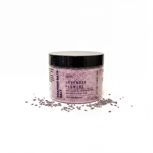 A jar of lavender bath salt surrounded by scattered lavender petals on a white background.