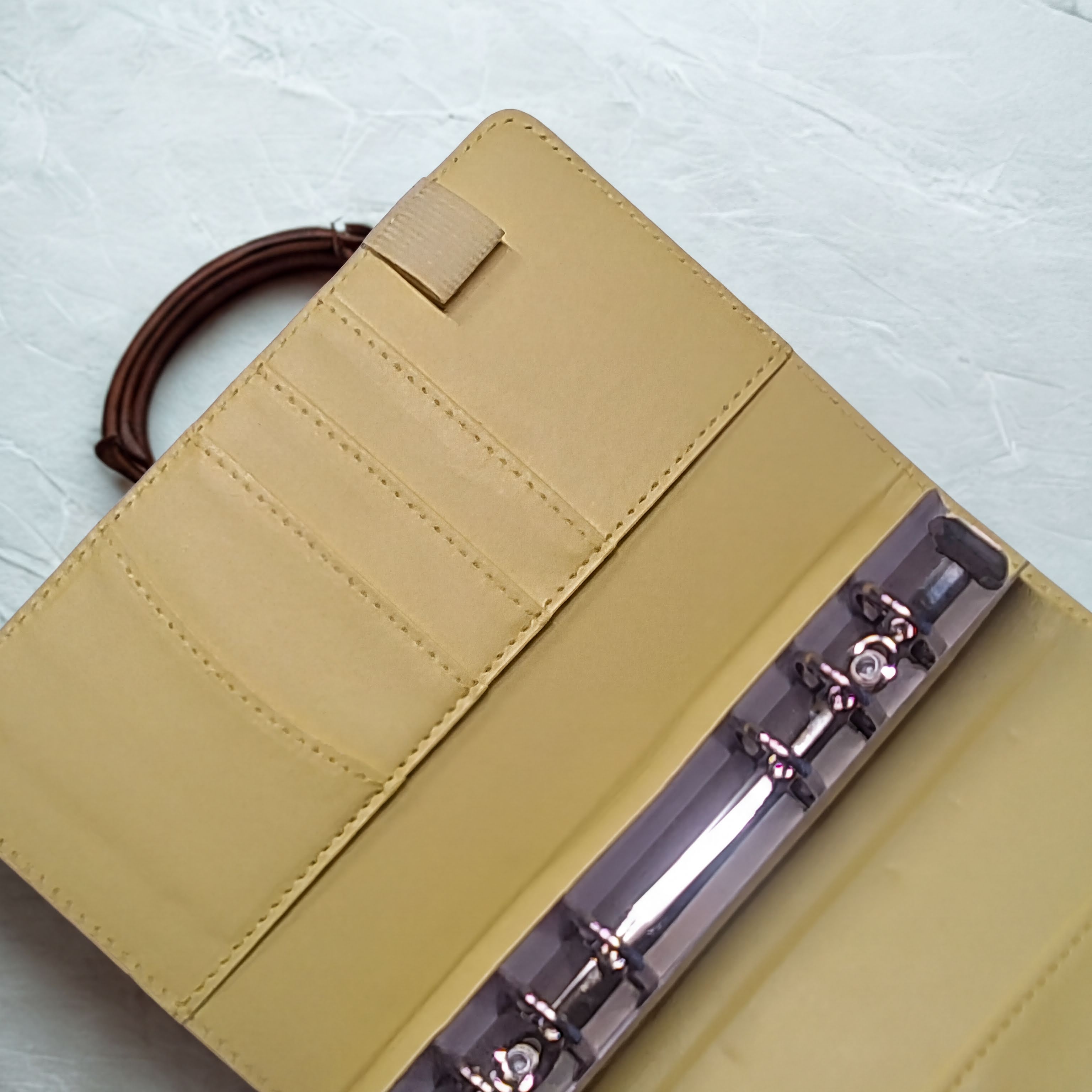 Tan leather wallet with card slots and metal clasp, on textured white surface