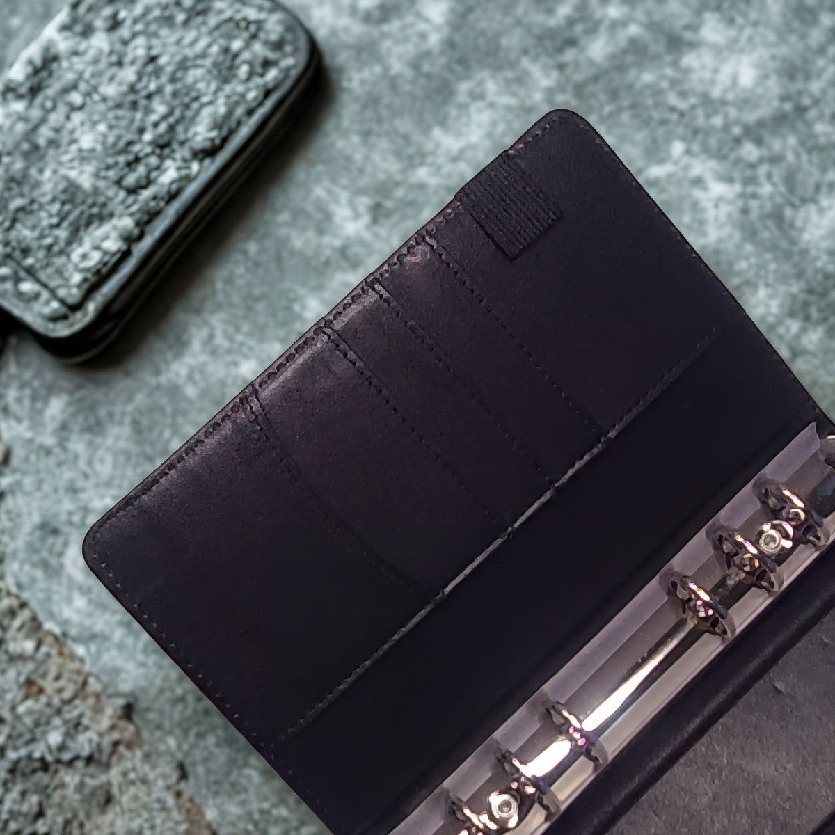Black leather wallet with card slots and metal rings on textured stone surface