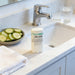 A bathroom counter with a cucumber slice dish, a bottle of cucumber splash deodorant, and a glass of water.