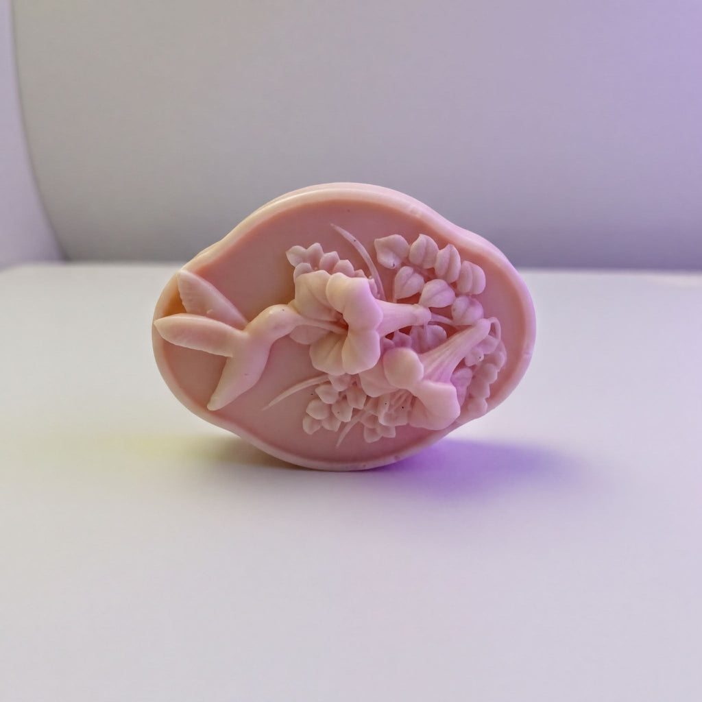 A pink soap bar with a floral design on it, sitting on a white surface.