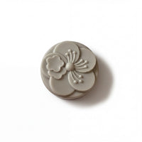 A gray, circular soap with a flower design on it.