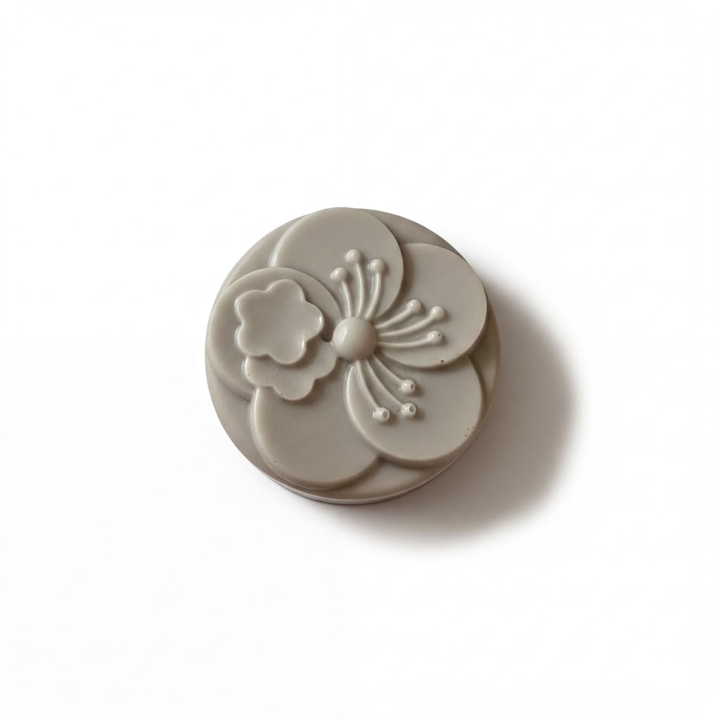 A gray, circular soap with a flower design on it.