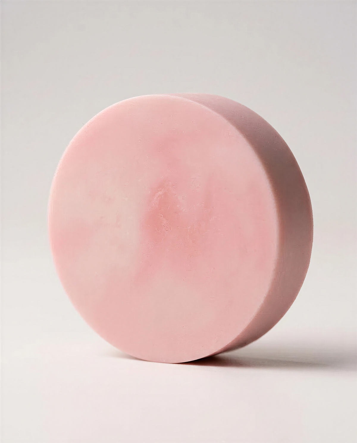 A round, pink soap bar is shown against a plain white background.