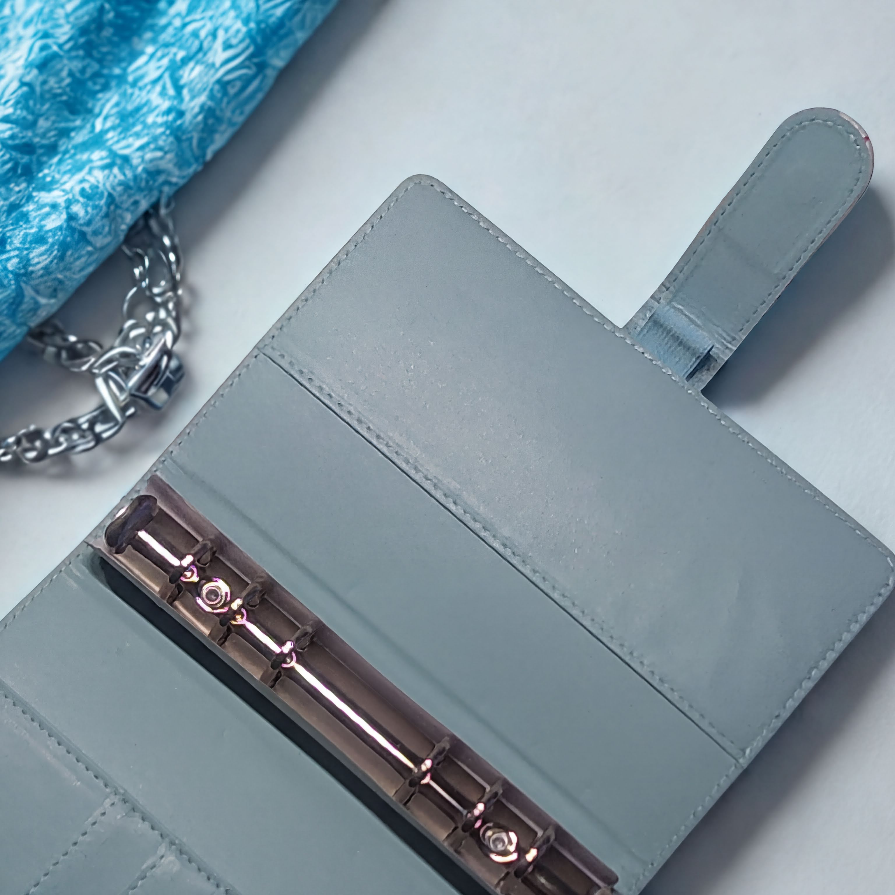 Light blue leather journal with rose gold rings, beside a blue velvet pouch with chain strap