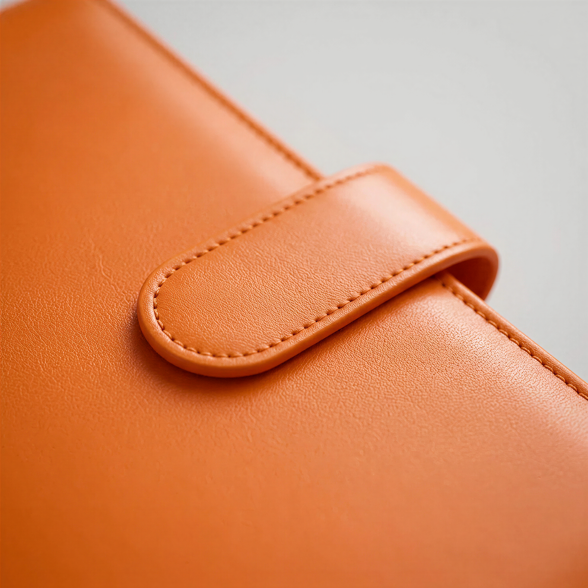 A close-up view of an orange leather wallet or book cover, with a curved zipper or clasp visible.