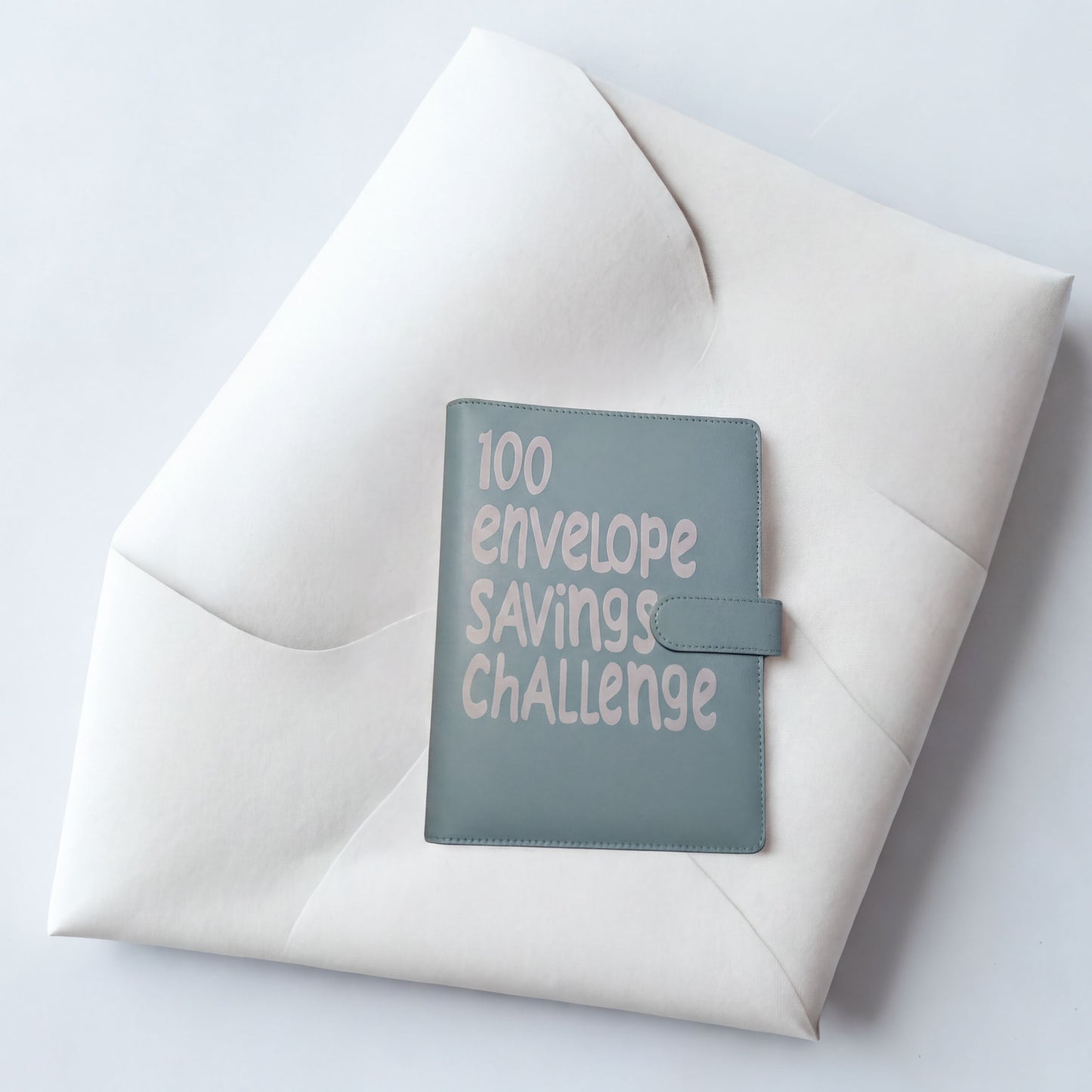 A light blue envelope with the text "100 envelope savings challenge" printed on it, placed on a white surface.