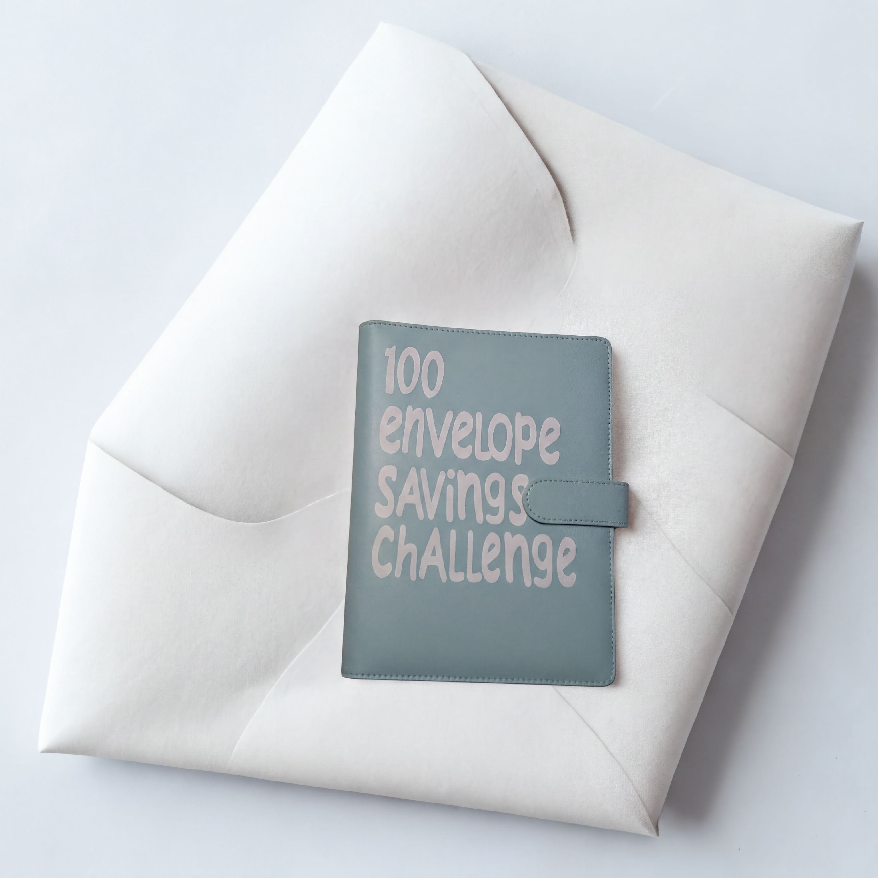 100 envelope savings challenge journal on white fabric background