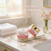 two jars of Sweet Pea Body Cream placed on a bathroom counter, with a vase of pink flowers nearby.