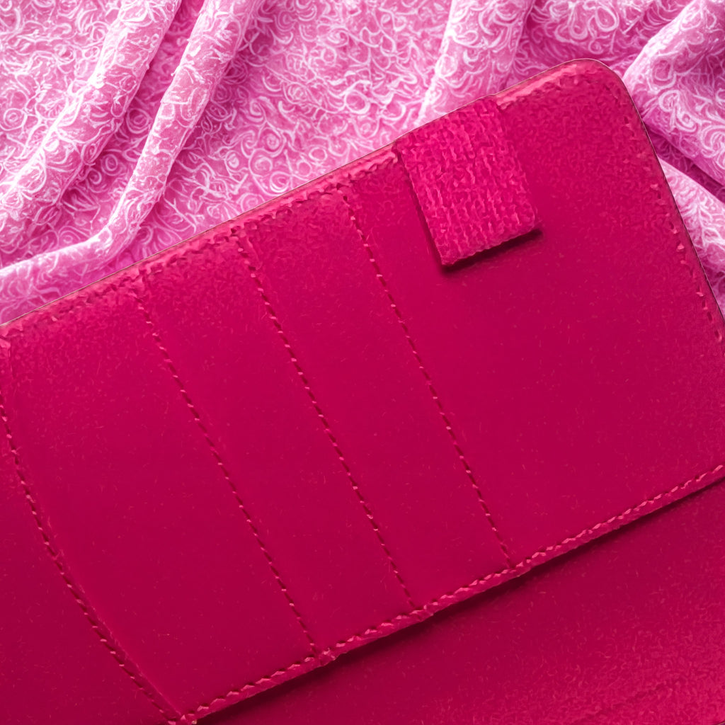 Vibrant pink leather wallet with neat stitching, set against a floral fabric background
