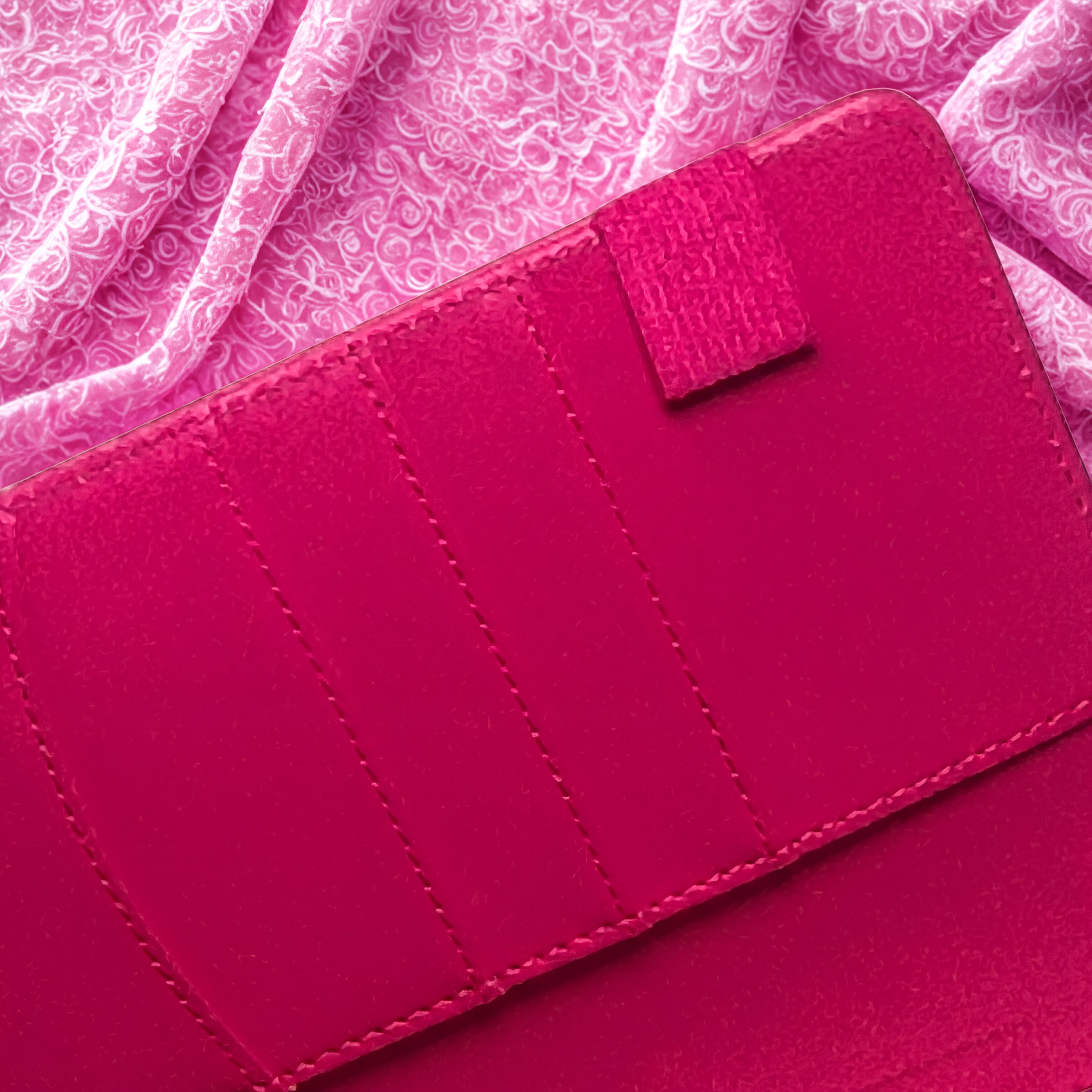 Vibrant pink leather wallet with neat stitching, set against a floral fabric background
