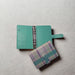 a mint green binder with a silver ring and a plaid wallet placed on a white surface.