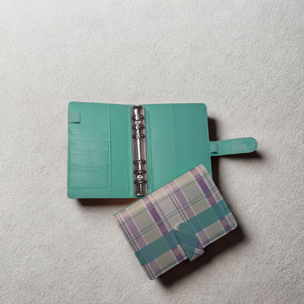 Mint green planner with plaid cover, open to show rings and pockets on textured white surface
