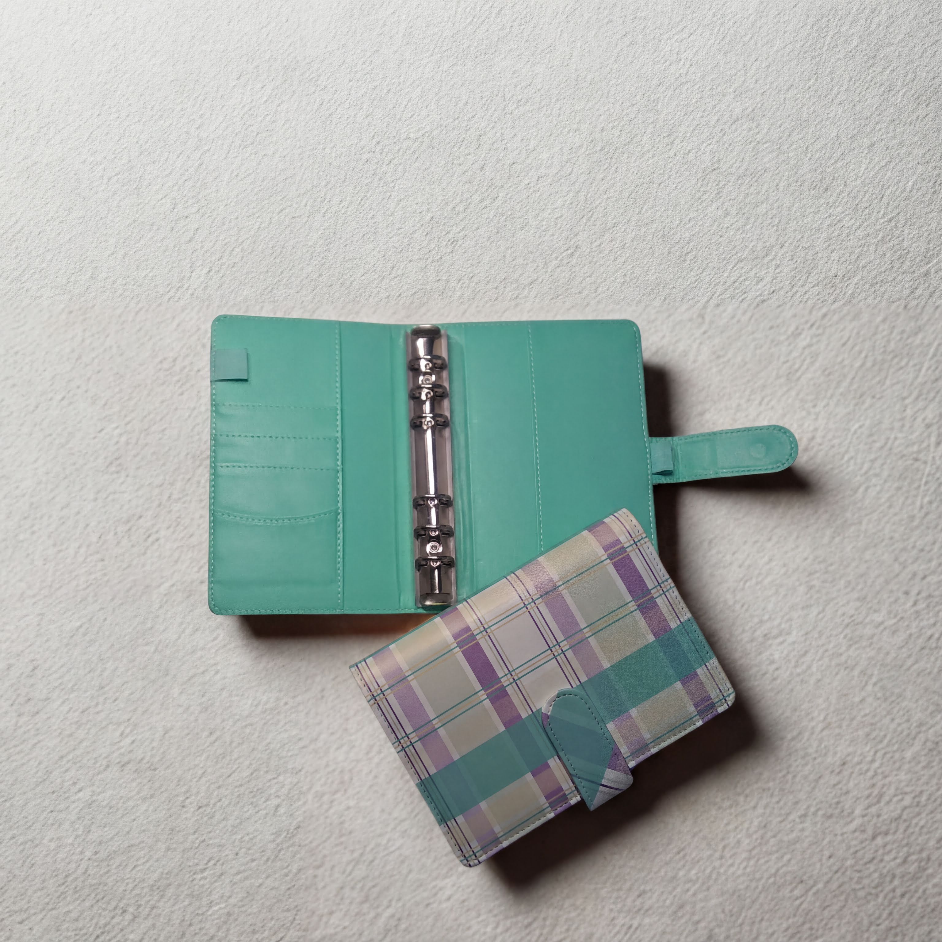 Mint green planner with plaid cover, open to show rings and pockets on textured white surface