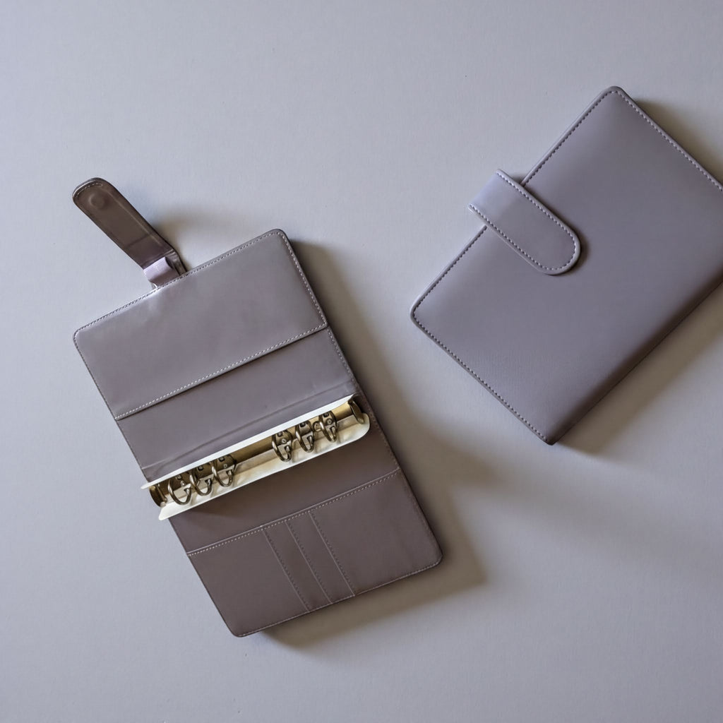 two gray leather wallets or purses placed on a light-colored surface.