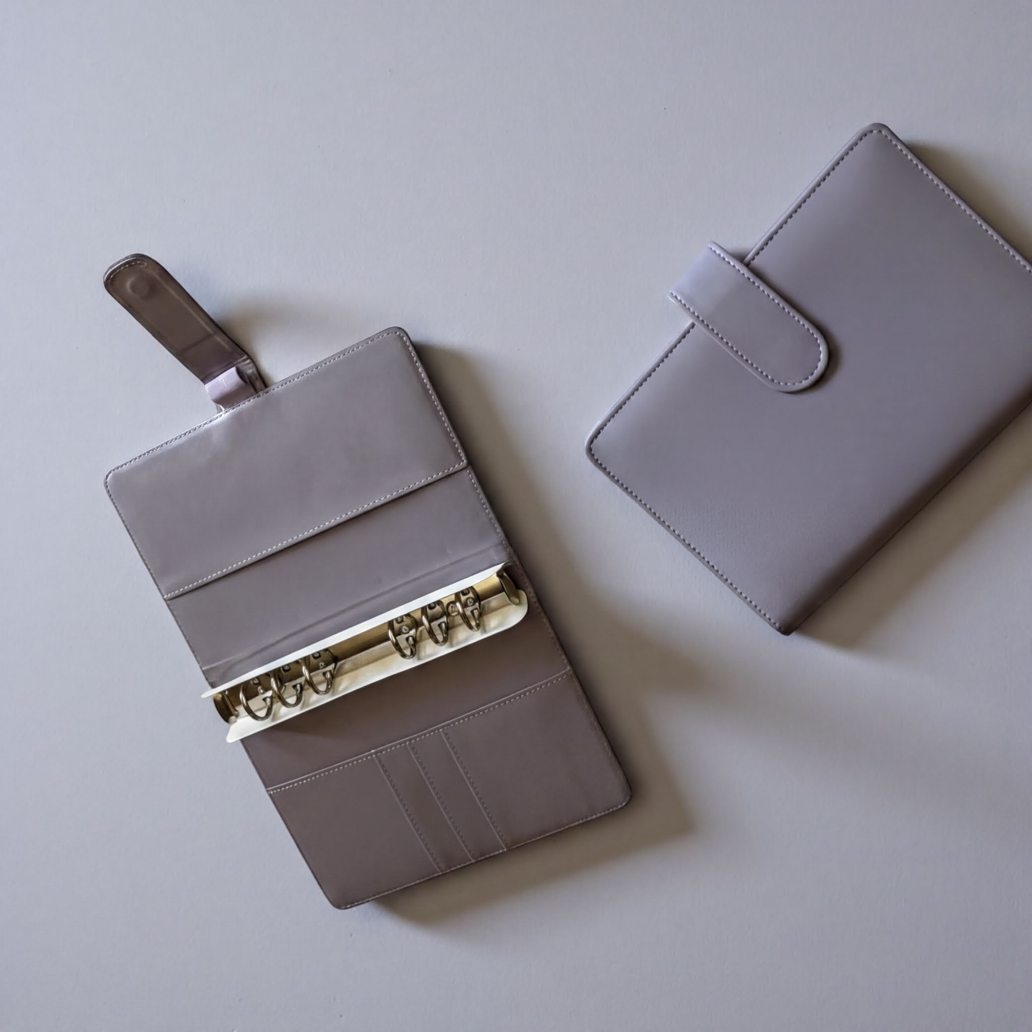 two gray leather wallets or purses placed on a light-colored surface.